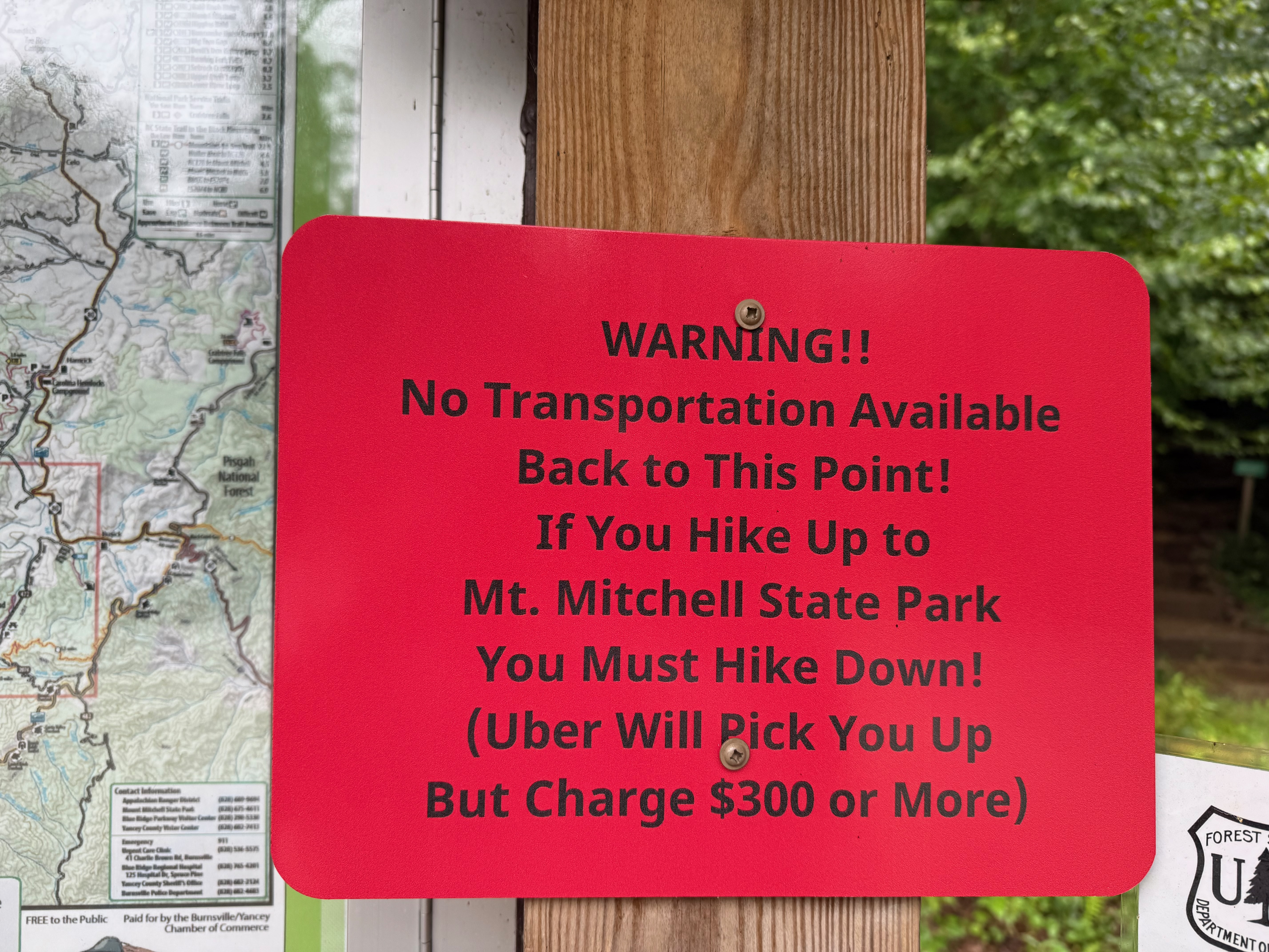 Warning sign indicating no transportation available back to this point for hikers at Mt. Mitchell State Park, with instructions to hike down and a note about high Uber charges.